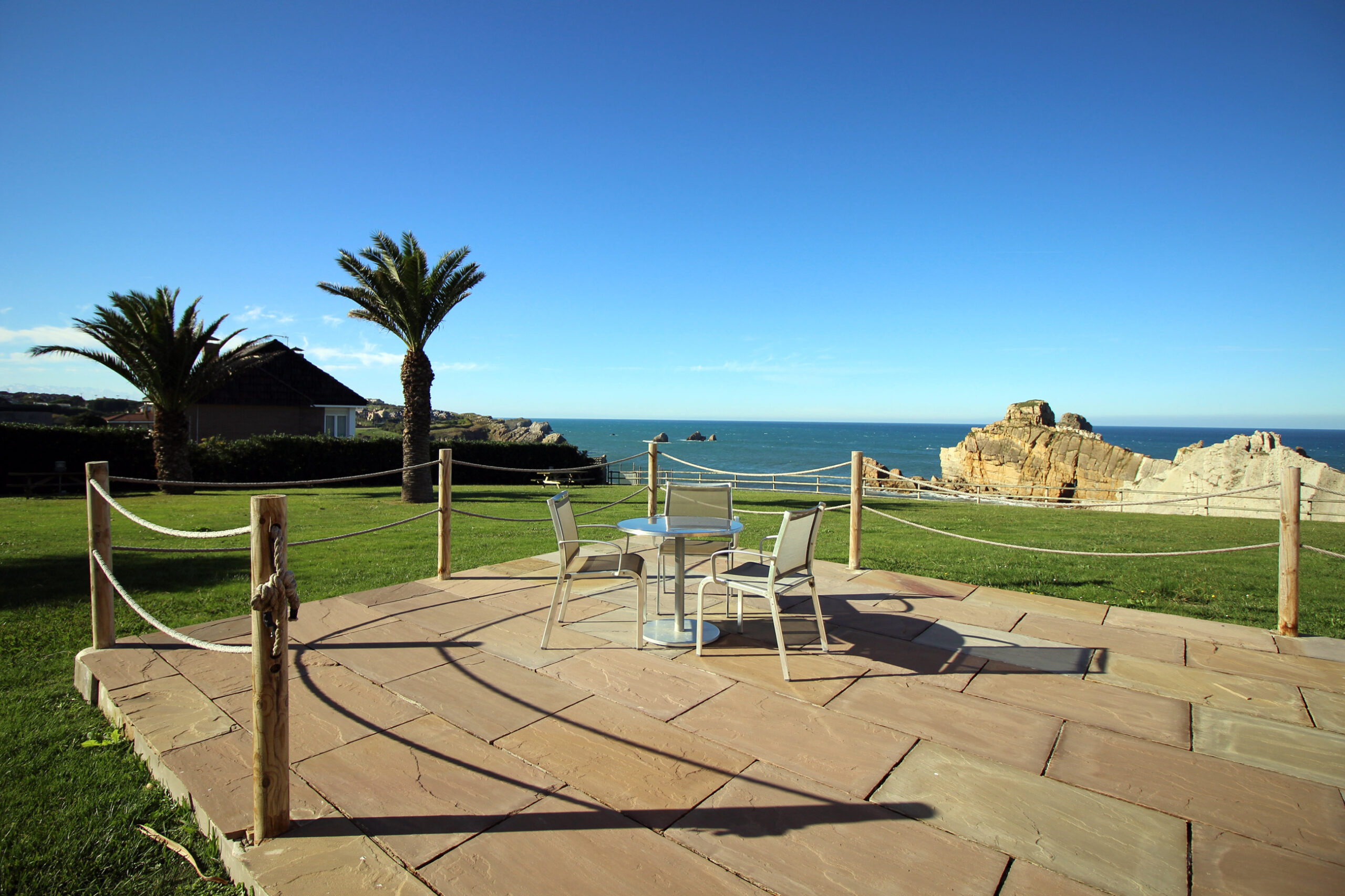 imagen del exterior de la posada con dos mesas de exterior junto a una mesilla y el mar de fondo